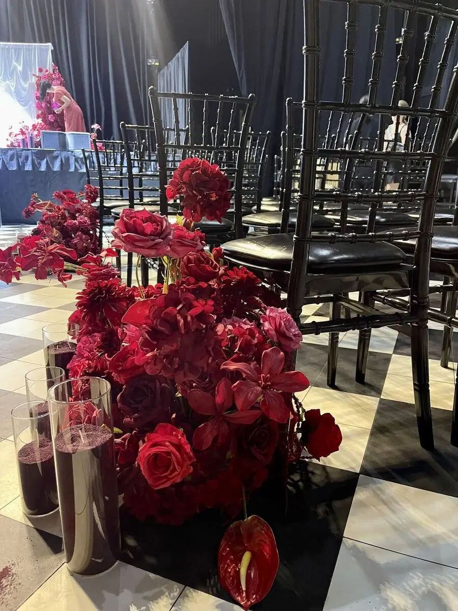 Black chiavari chairs and a rich red floral installation on a checkerboard dance floor.