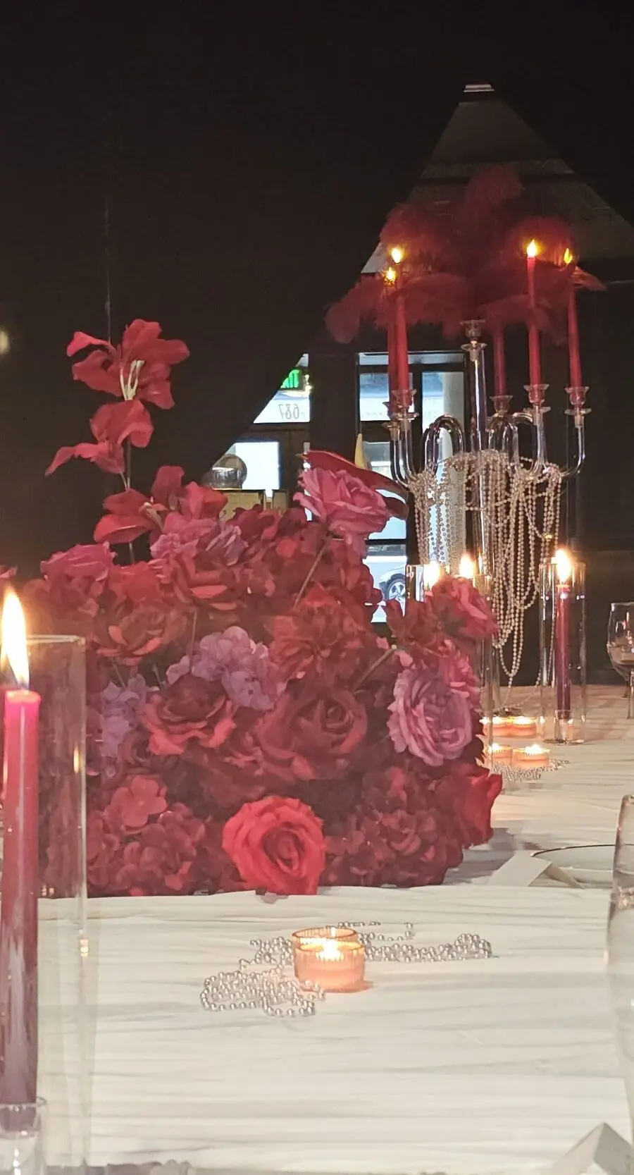 Feathered candelabra with red candles and cascading pearls at a luxury gala tablescape.