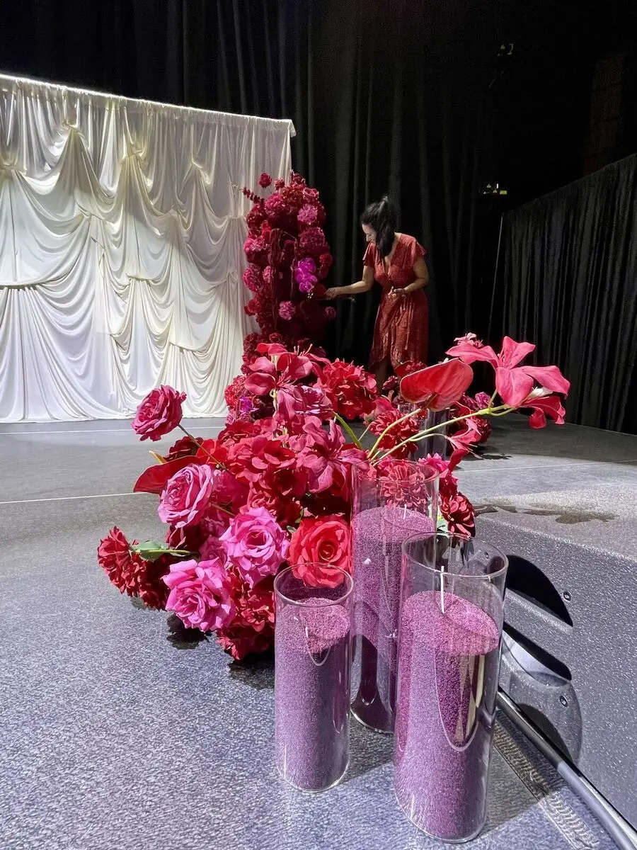 Deep red floral arrangement beside black chiavari chairs on a black and white checkerboard floor.