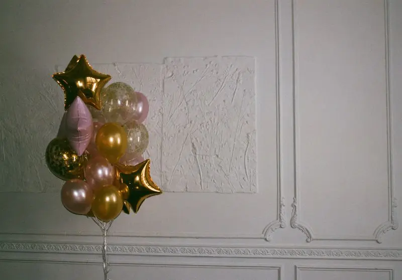 Gold and pink balloons forming a decorative bouquet against a textured white wall.