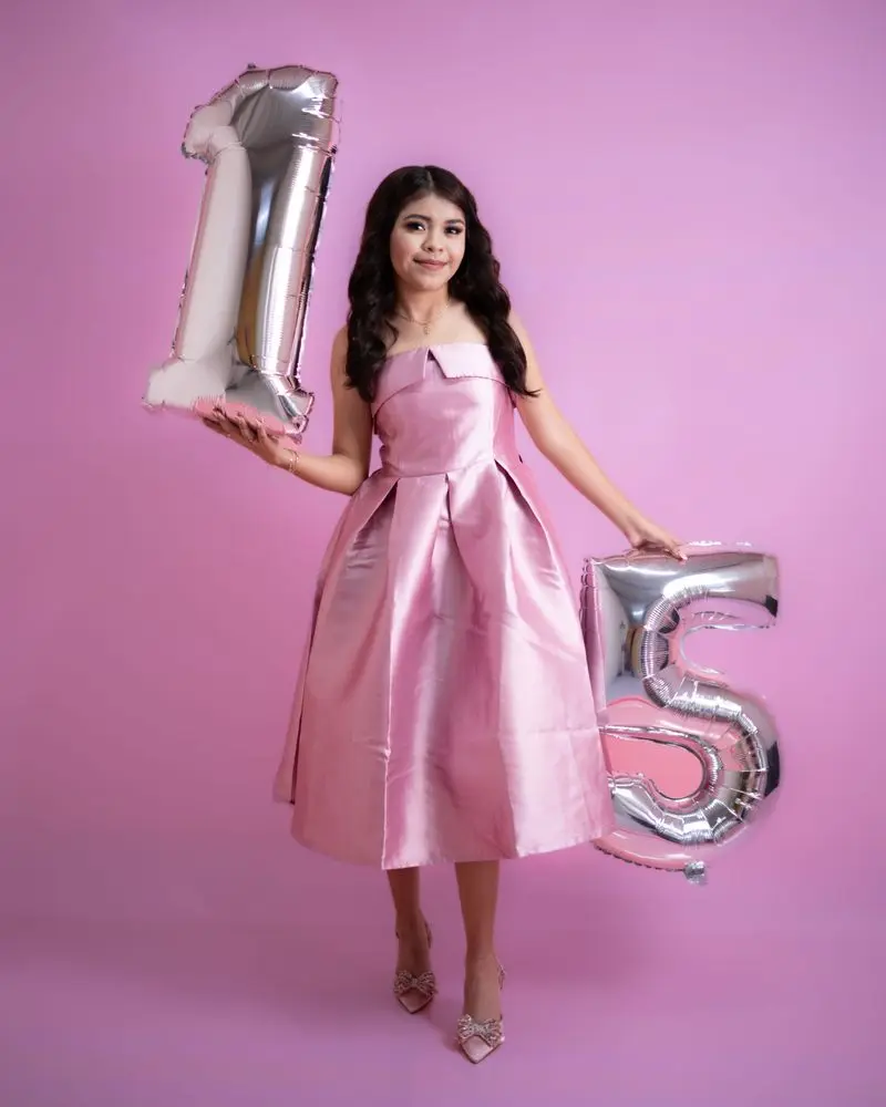 Teenage girl in pink dress holding silver number balloons for a quinceañera.