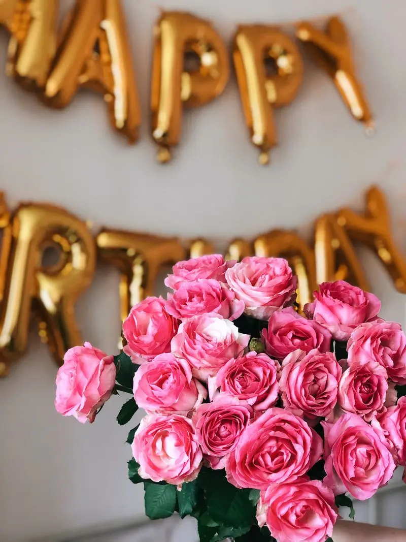 A stunning bouquet of pink roses at a birthday party with golden balloons spelling 'Happy Birthday' in the background.